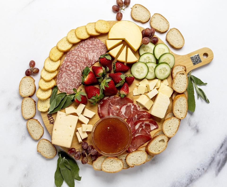 round brown paddle cheese board with cheese, crackers, and sliced meat