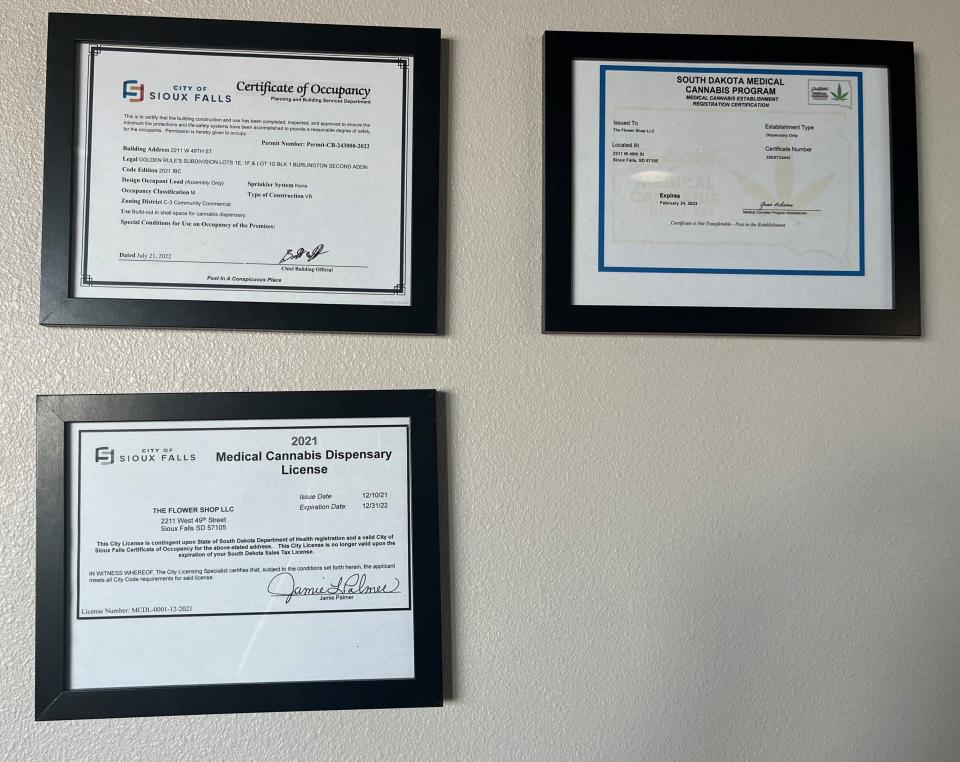 Flower Shop Dispensary displays the three types of licenses it needs in order to operate: a certificate of occupancy, a medical cannabis dispensary license from the City of Sioux Falls, and a South Dakota Medical Cannabis Establishment Registration Certification.