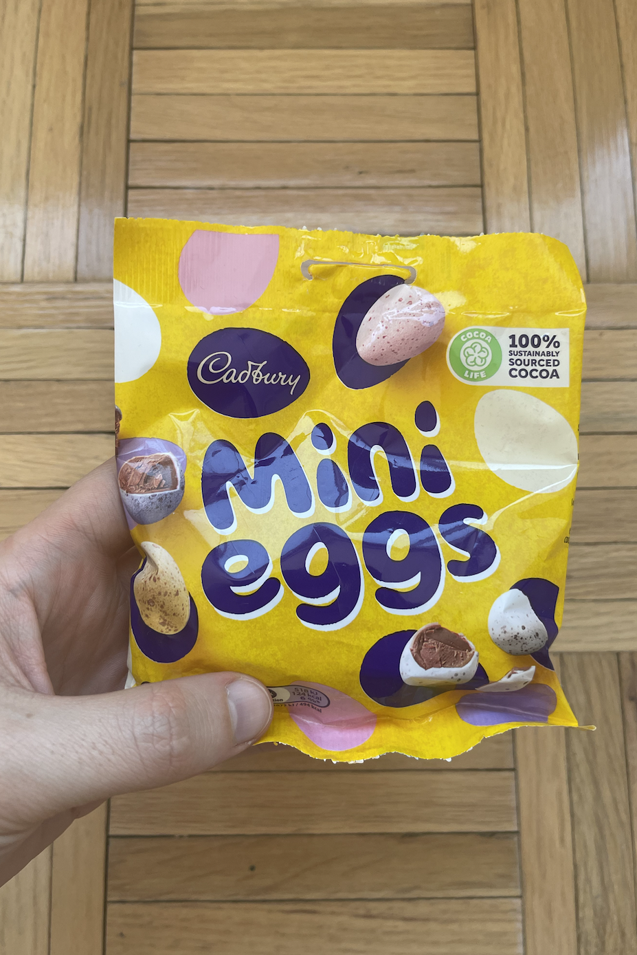 Hand holding an open Cadbury Mini Eggs candy package, showing the candies inside