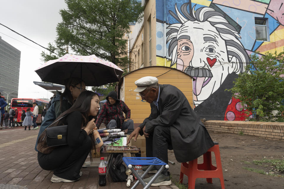 FILE - A Mongolian woman consults a fortuneteller divining fortunes with stones on a street across from Sukhbaatar Square in Ulaanbaatar, Mongolia on Thursday, June 27, 2024. The proportion of female representatives rose from 17% to 25% in the new elected parliament, but most of those came in 48 seats that are allocated to parties based on their share of the vote. (AP Photo/Ng Han Guan, File)