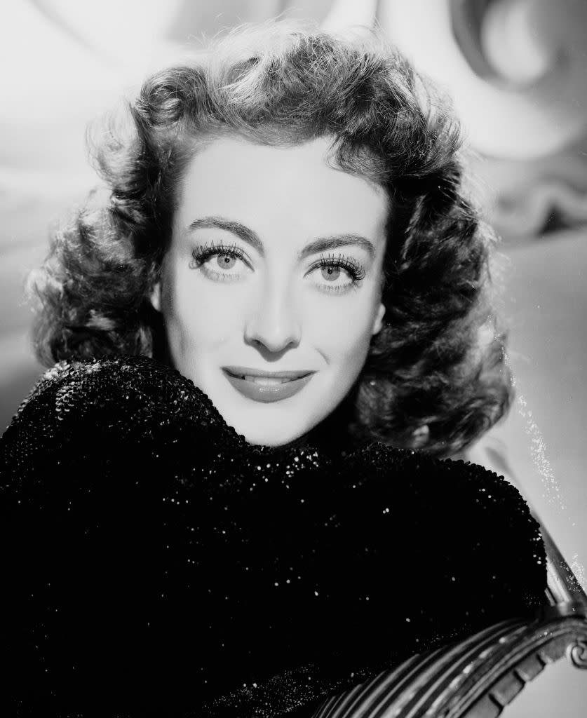 Joan Crawford smiling, wearing a sparkling, textured top; her hair styled in soft curls