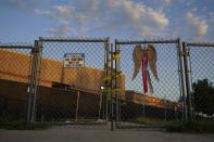 Angel wings and a cross hang on a gate that remains locked at Robb Elementary School where two teachers and 19 students are killed recently, Monday, July 11, 2022, in Uvalde, Texas. A Texas lawmaker says surveillance video from the school hallway where police waited as a gunman opened fire in a fourth-grade classroom will be shown this weekend to residents of Uvalde(AP Photo/Eric Gay)