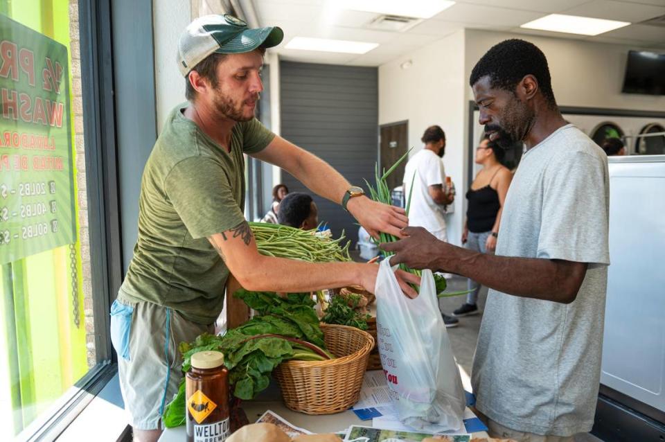Ben Carpenter places a bundle of green onions into Byron Kirkwood’s bag during Community Laundry Day at Leah’s Laundromat on the Q, Carpenter is the New Roots for Refugees Education and Outreach Coordinator and helps provide free produce for customers during the monthly event.