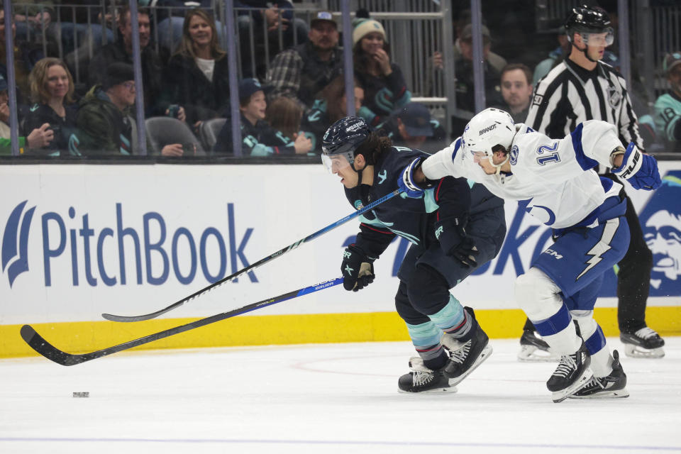 Seattle Kraken left wing Brandon Tanev (13) and Tampa Bay Lightning center Alex Barre-Boulet (12) compete for the puck during the first period of an NHL hockey game Saturday, Dec. 9, 2023, in Seattle. (AP Photo/Jason Redmond)