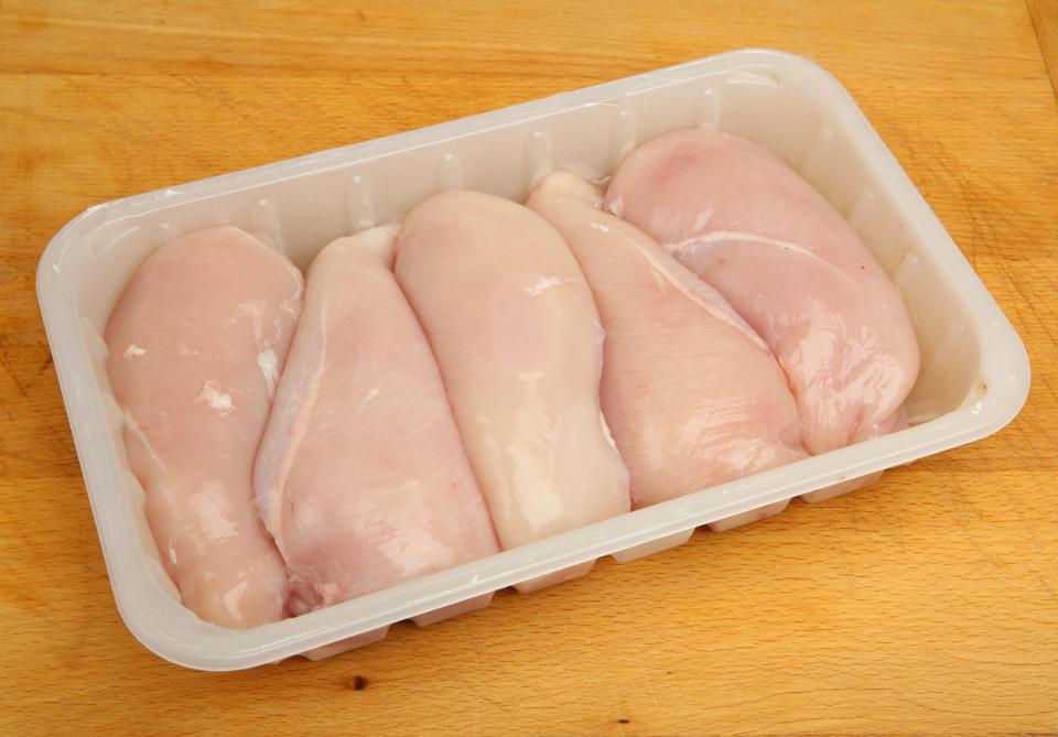 Five raw chicken breasts in a white container on a wooden counter
