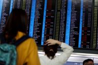 Passengers react as they look at the flight information board as the airport reopened a day after flights were halted due to a protest, at Hong Kong International Airport, China