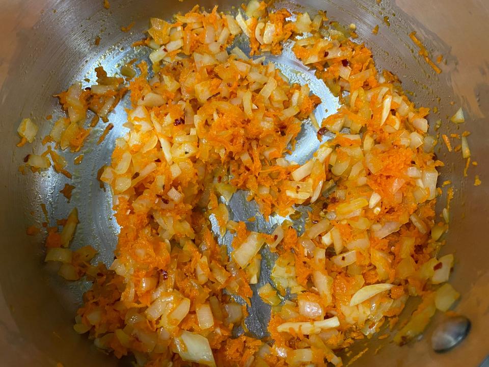 Onion, garlic, and shredded carrot sautéing in a pan