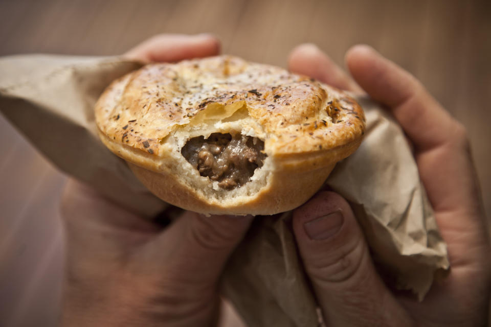 Close-up of a man's hands holding an Australian meat pie with a bite taken out of it