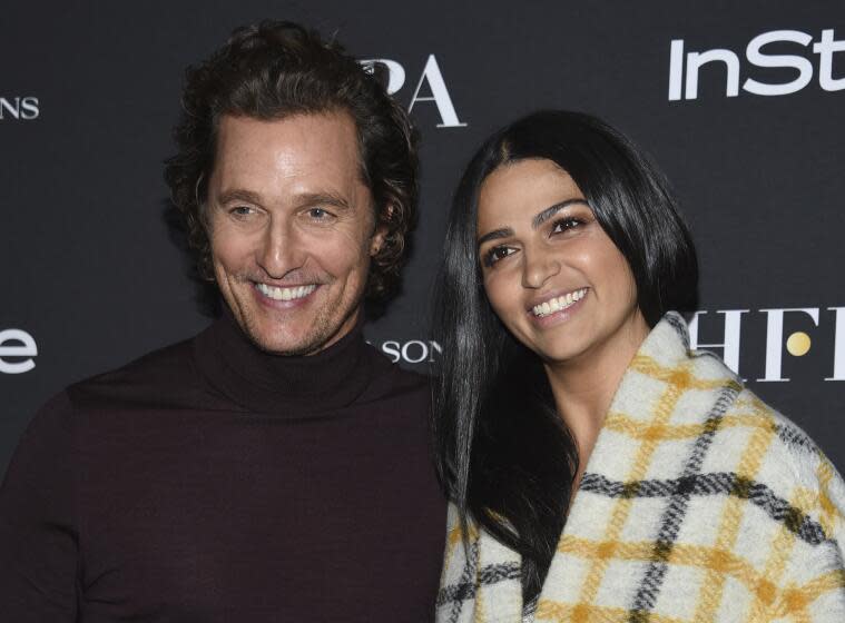 Matthew McConaughey smiling in a purple turtleneck next to Camila Alves in a plaid blanket