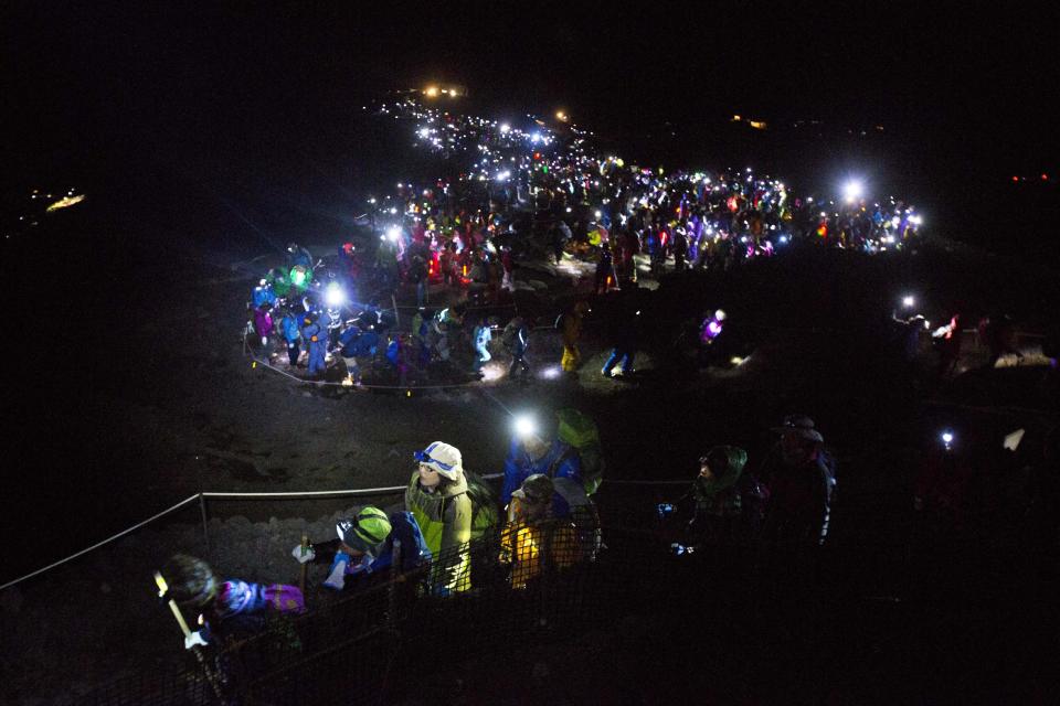 In this Sunday, Aug. 11, 2013 photo, thousands of hikers, with headlamps and flashlights lighting their way, climb to the summit of Mount Fuji in Japan before dawn. The recent recognition of the 3,776-meter (12,388-foot) peak as a UNESCO World Heritage site has many here worried that will draw still more people, adding to the wear and tear on the environment from the more than 300,000 who already climb the mountain each year. (AP Photo/David Guttenfelder)