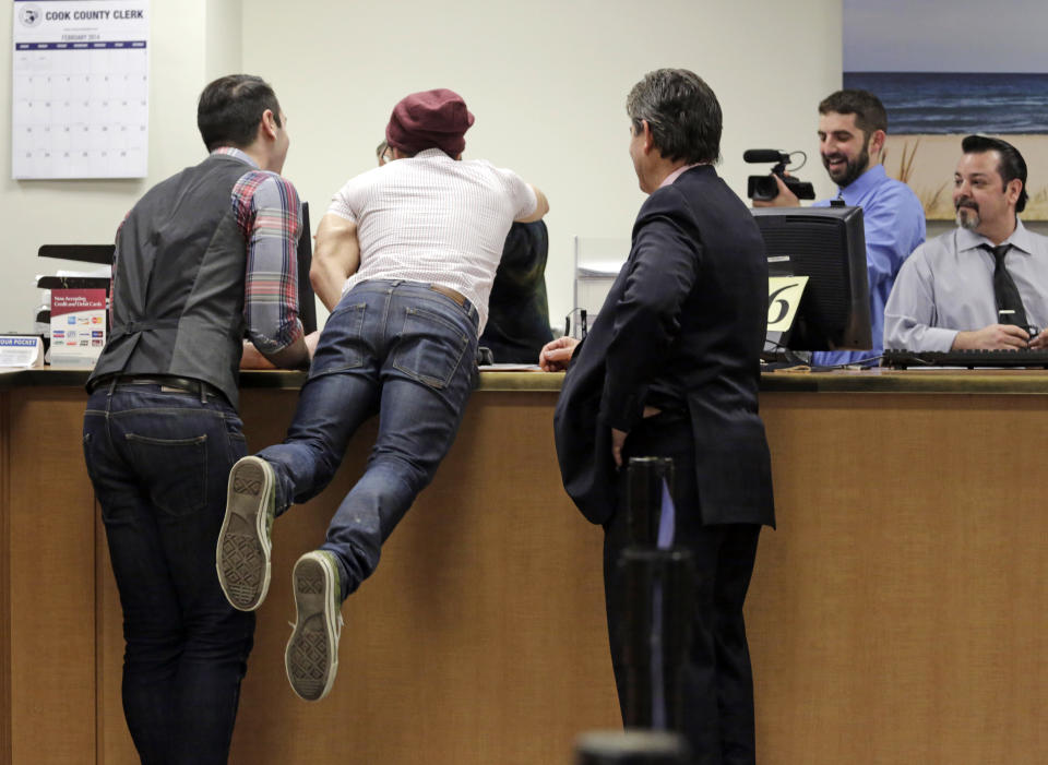 David Wilk leaps across the counter to hug Cook County Clerk's office employee Louisa Nicotera after obtaining a marriage license with partner Charlie Gurion, left, Friday, Feb. 21, 2014, in Chicago. Same-sex couples in Illinois' Cook County began receiving marriage licenses immediately after a federal judge's ruling Friday that some attorneys could give county clerks statewide justification to also issue the documents right away. (AP Photo/M. Spencer Green)