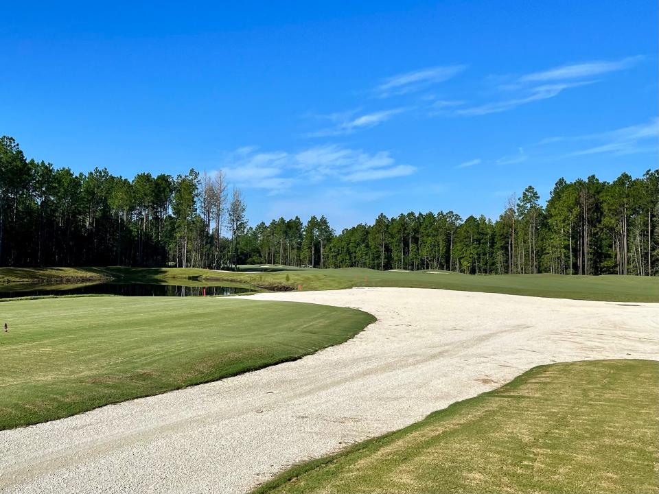 The first hole of the Stillwater Golf Course features a meandering fairway, framed by tall pine trees and bordered down the left side by water.