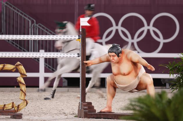 A show jumper rides behind an obstacle with a sumo wrestler beside it in an event at the Tokyo Olympics. (Photo: picture alliance via Getty Images)