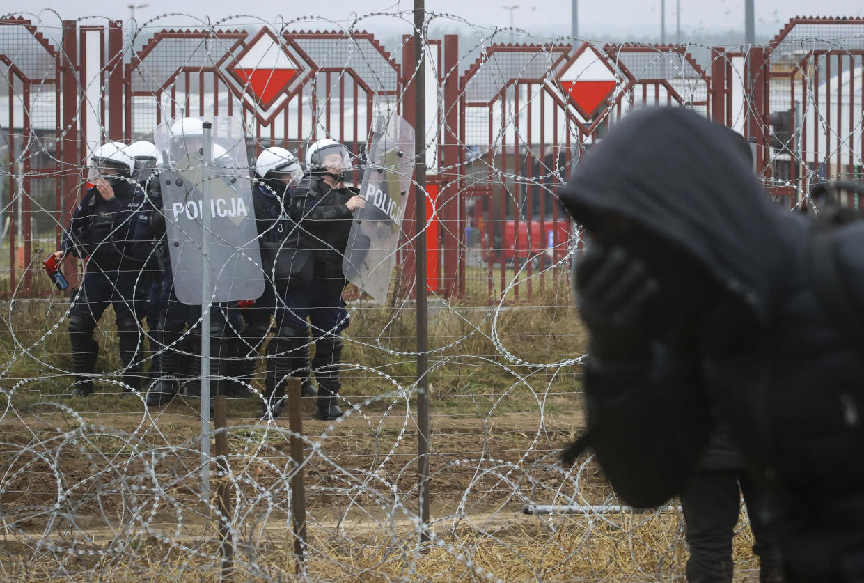 Polish servicemen are seen on the other side of barbed wire during clashes between migrants and Polish border guards at the Belarus-Poland border near Grodno, Belarus, on Tuesday, Nov. 16, 2021. Polish border forces say they were attacked with stones by migrants at the border with Belarus and responded with a water cannon. The Border Guard agency posted video on Twitter showing the water cannon being directed across the border at a group of migrants in a makeshift camp. (Leonid Shcheglov/BelTA via AP)