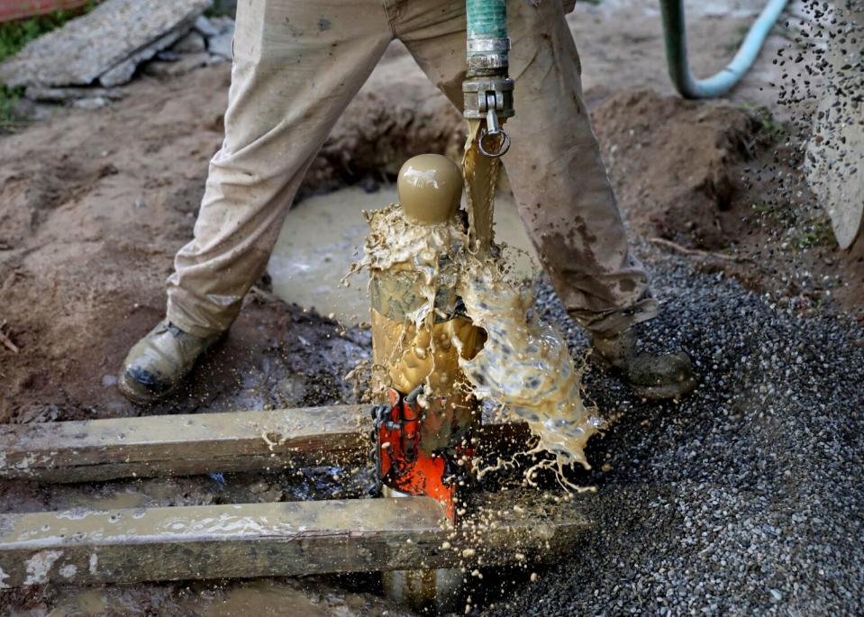 Dirty water splashes out of a hose as a person seen from the waist down drills a well.