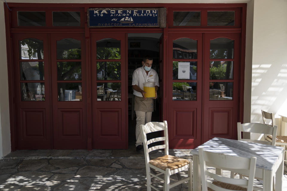 A Doryssa hotel employ wearing a protective face mask carries orange juice as he exits a coffee shop on the eastern Aegean island of Samos, Greece, Tuesday, June 8, 2021. About a month after Greece officially opened to international visitors, the uncertainty of travel during a pandemic is still taking its toll on the country's vital tourist industry. (AP Photo/Petros Giannakouris)