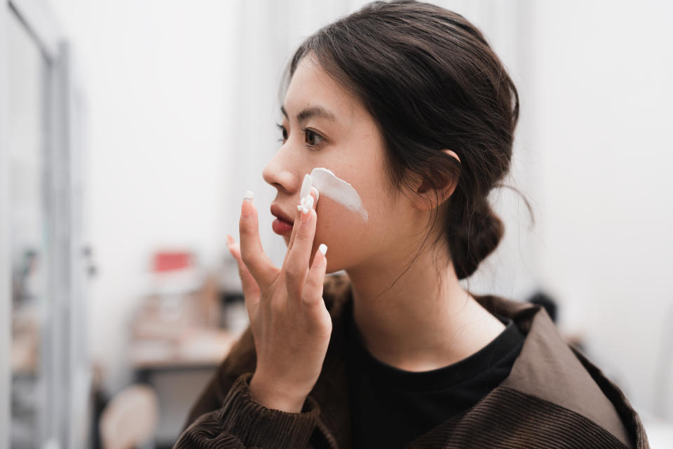 An Asian girl looks into the mirror and applies makeup to her face with her hands