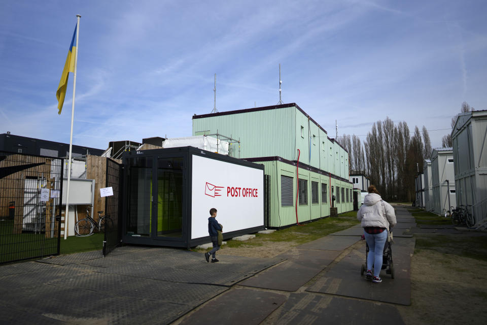 A woman and a boy walk by a container post office at the Ukraine village, which has been constructed for Ukrainian families fleeing the war, in Linkeroever, Belgium, Friday, March 17, 2023. Despite the warm welcome for millions of Ukraine refugees on European Union soil since the Russian invasion, EU officials said Tuesday, June 6, 2023 that there are some fears of wavering support caused by a bad economy hitting poor families especially and the creeping influence of Russian propaganda. (AP Photo/Virginia Mayo)
