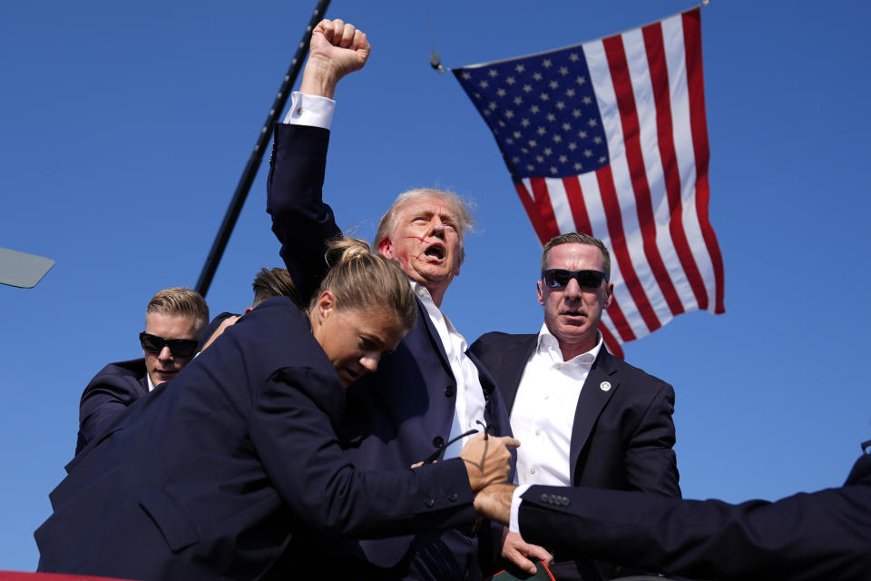 Donald Trump with apparent blood on his face is surrounded by Secret Service agents whisking him off stage.