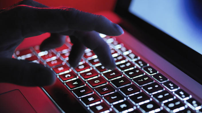 Dimly lit fingers hover over a back-lit laptop keyboard.