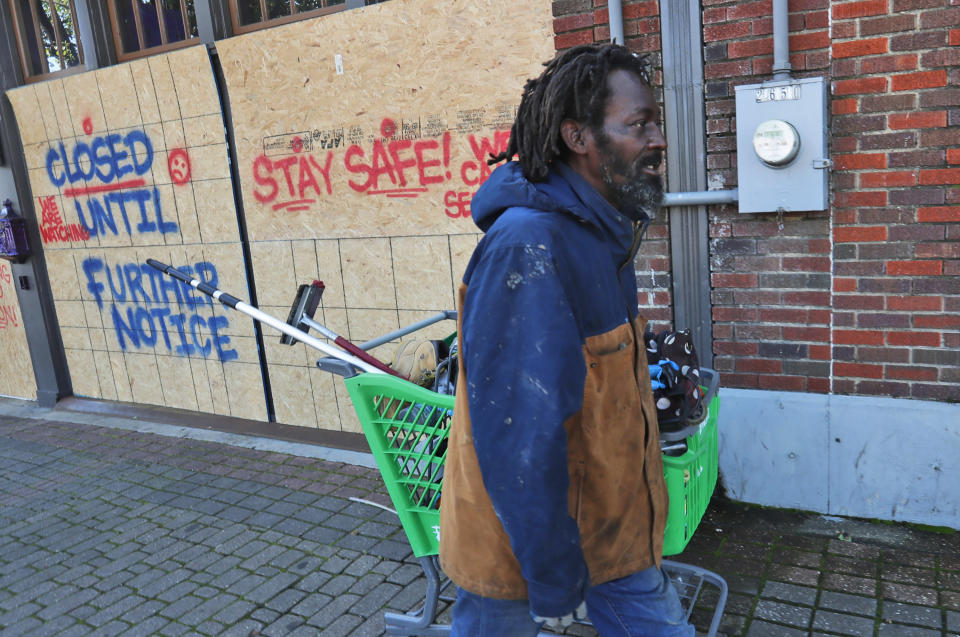 FILE - In this Tuesday, March 31, 2020 file photo, Vincent Amos, who identified himself as homeless, pulls a shopping cart with his belongings amid businesses closed by concerns of the COVID-19 coronavirus in the Deep Ellum section of Dallas. Amos said his shelter in place routine includes walking the area looking for work cleaning windows. (AP Photo/LM Otero)