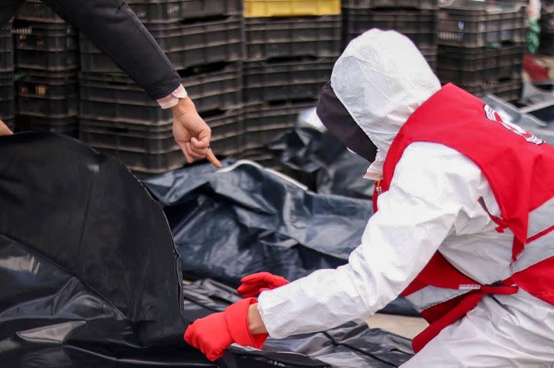 Libyan Red Crescent worker puts the body of a migrant, who died after their boat capsized, in a bag, in Garabulli