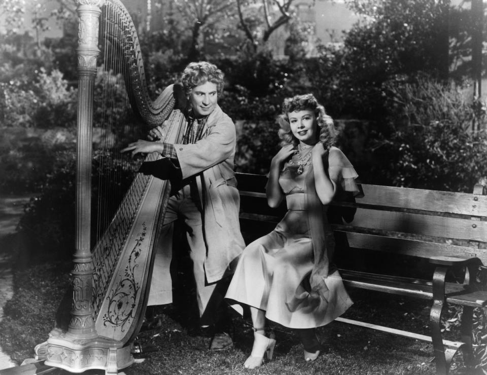 Harpo Marx playing the harp for Vera Ellen in a scene from the film 'Love Happy', 1949