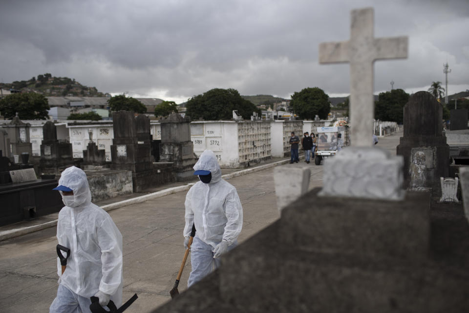 FILE - In this April 13, 2021, file photo, cemetery workers in protective gear walk to the burial of a woman who died from complications related to COVID-19 at the Inahuma cemetery in Rio de Janeiro, Brazil. The picture is still grim in parts of Europe and Asia as variants of the virus fuel an increase in new cases and the worldwide death toll closes in on 3 million. (AP Photo/Silvia Izquierdo, File)