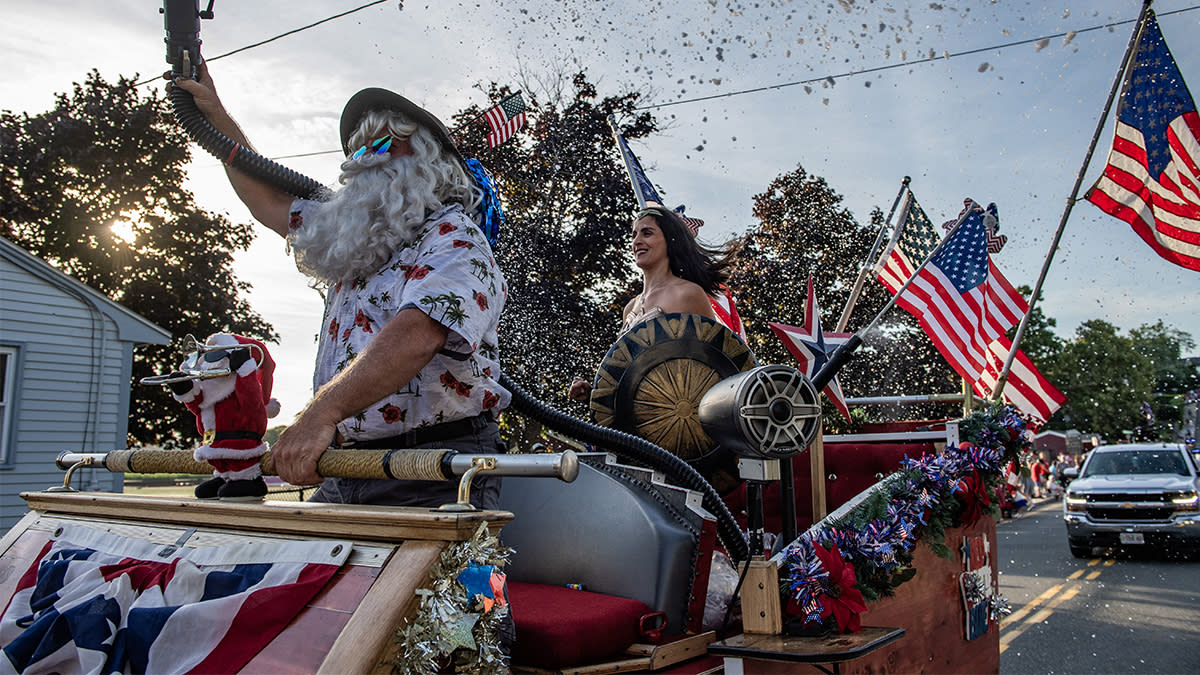 Des personnes déguisées en Père Noël et en Wonder Woman aspergent de fausse neige les participants à la Fishtown Horribles Parade, avant le Jour de l'Indépendance, à Gloucester, Massachusetts, le 3 juillet 2024. La parade fait partie des célébrations du 4 juillet de la ville. | Joseph Prezioso / AFP