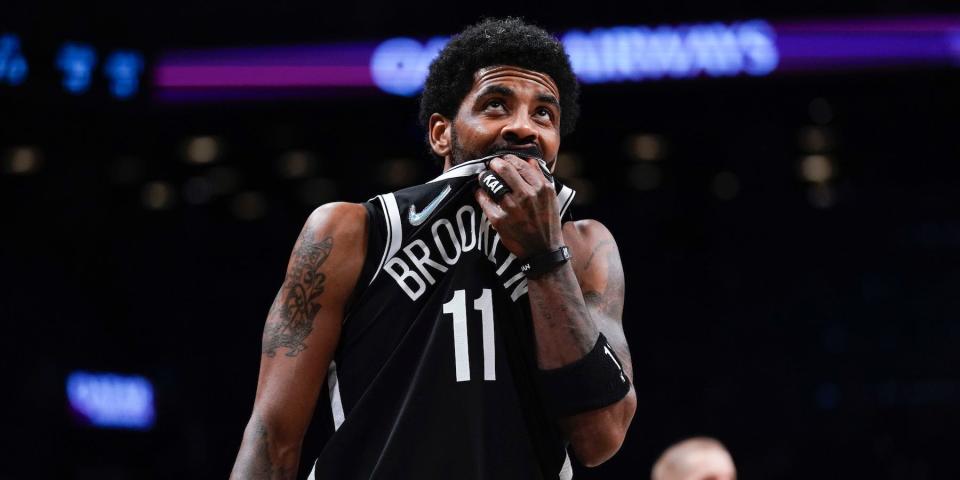 Kyrie Irving looks up and holds his jersey over his mouth during a Nets game in 2022.