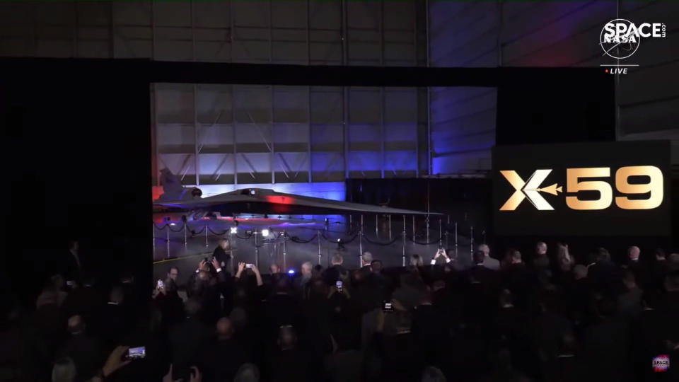 A crowd watches a sleek supersnic plane being unveiled in a hangar