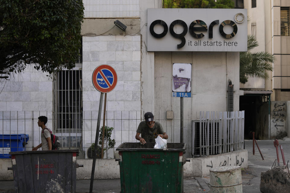 A man scavenges in the garbage next to a building of the state-owned telecom and internet company, Ogero, in Beirut, Lebanon, Wednesday, Aug. 31, 2022. Internet shutdowns rippled through cash-strapped Lebanon on Tuesday after employees of Ogero went on strike, demanding higher wages. (AP Photo/Hassan Ammar)