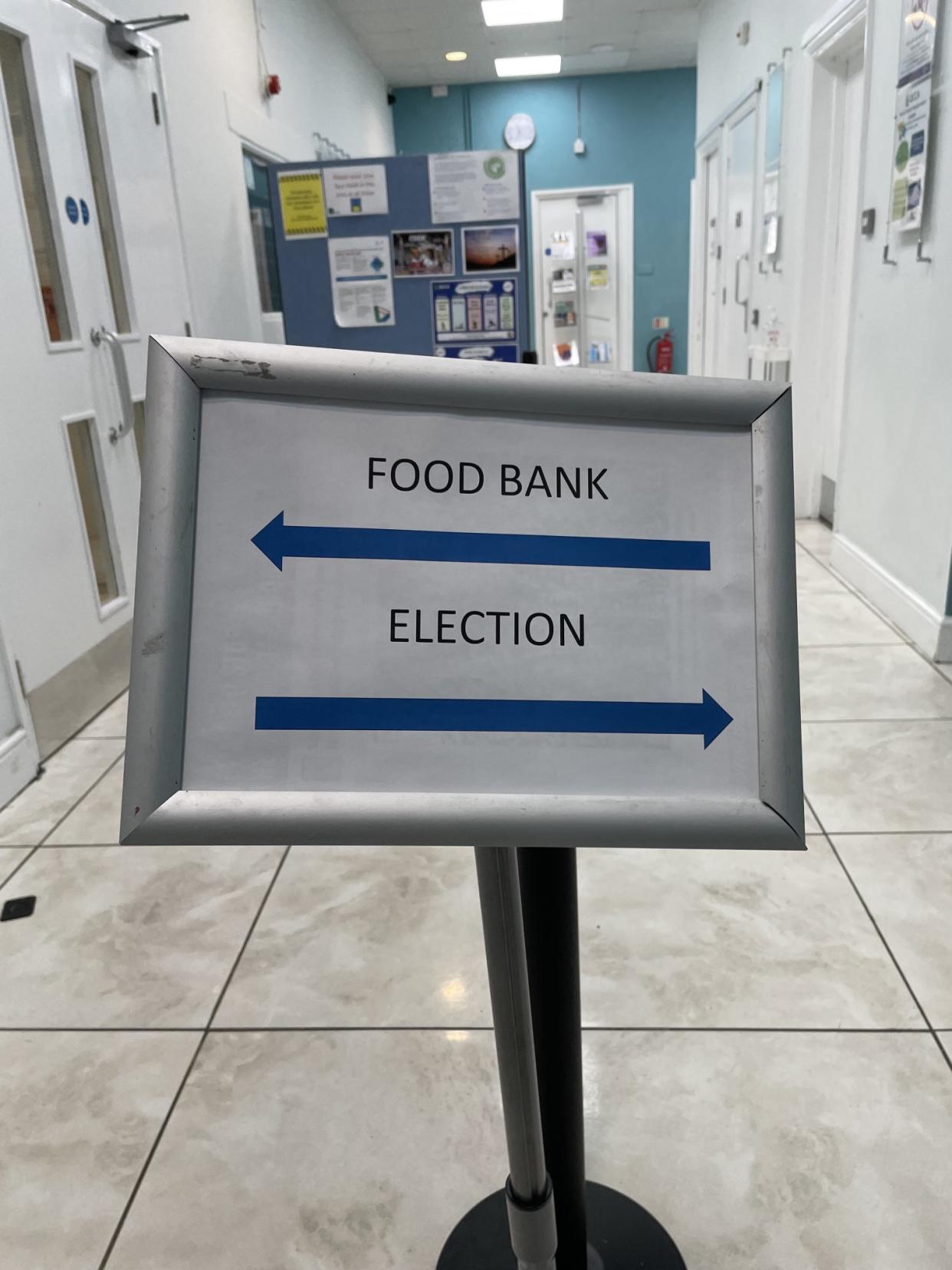 A sign at Queen's Crescent Community Association for a food bank in one direction and a polling station in the other. (Usman Khan/@healthandthings/Twitter)