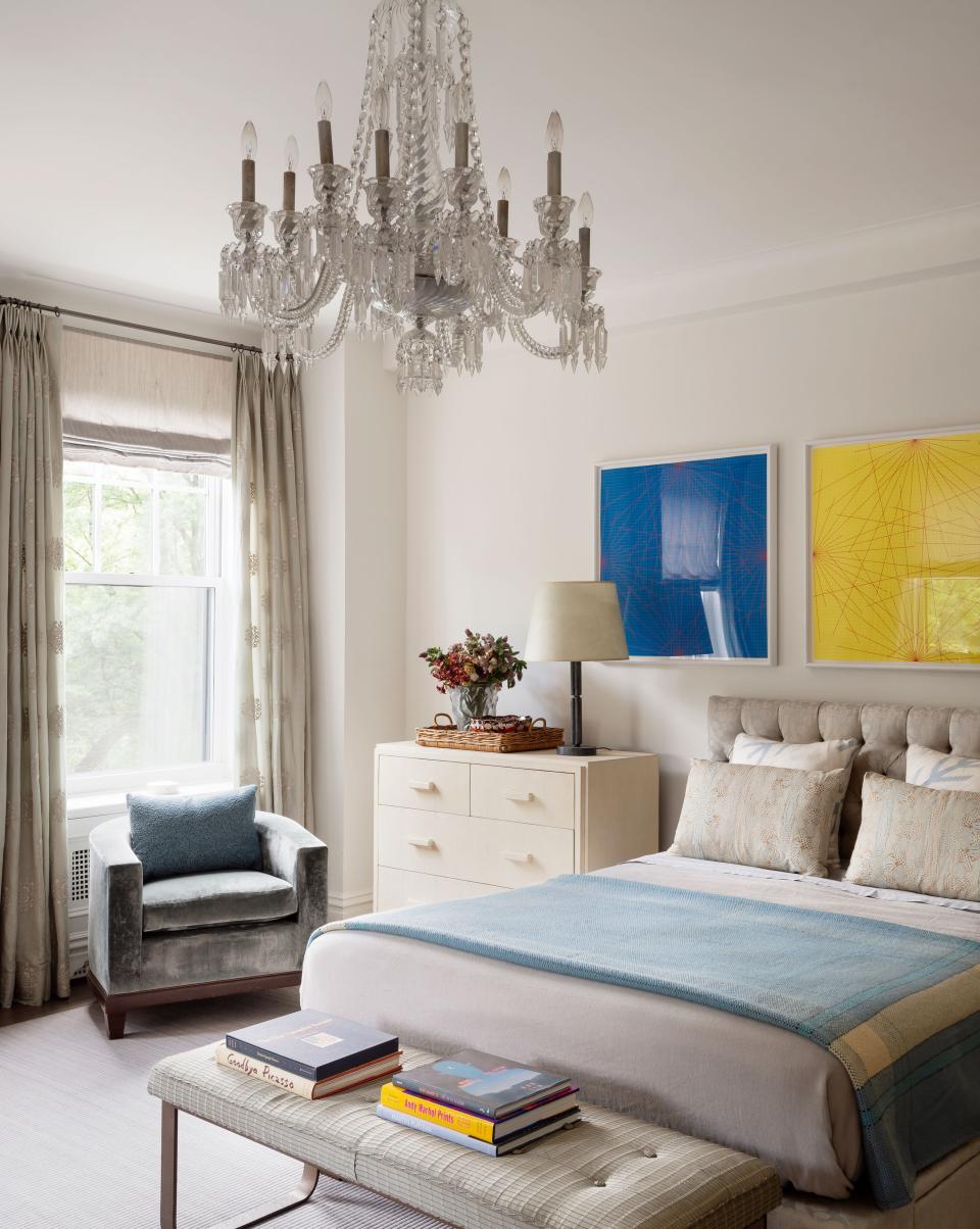The primary bedroom boasts a custom headboard outfitted in Rogers & Goffigon fabric as well as a custom brass bench upholstered Jerry Pair fabric. The white shagreen bedside dressers are from Donna Parker Antiques, the chandelier is antique Italian, and the artworks are by Sol LeWitt.