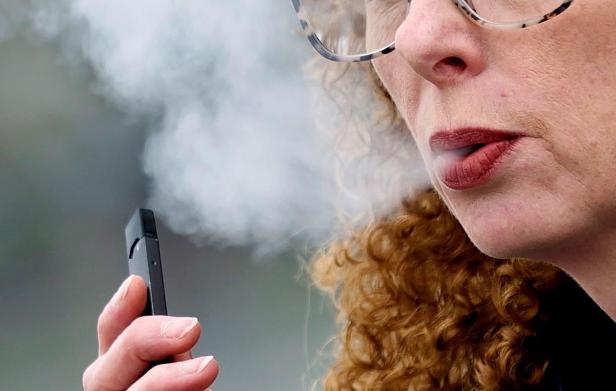A woman exhales while vaping from a Juul pen e-cigarette in Vancouver, Wash., April 16, 2019. 