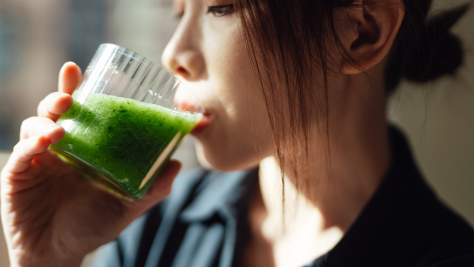 are powdered greens worth it: Young woman drinking a glass of fresh green fruit and vegetable smoothie with natural sunlight.