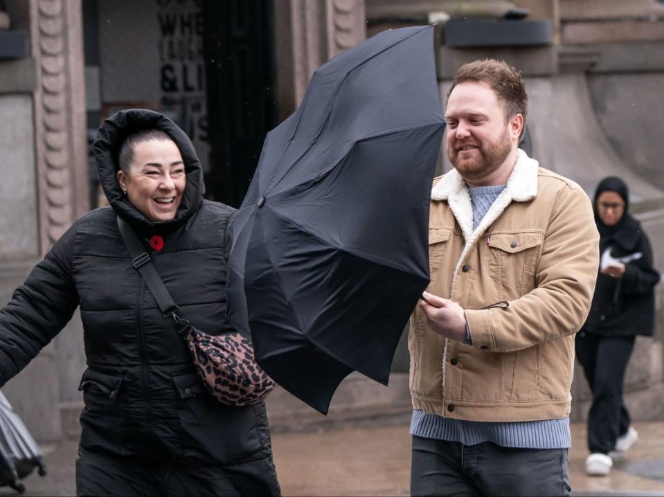 A man struggles with an umbrella in windy conditions in Leeds (PA)