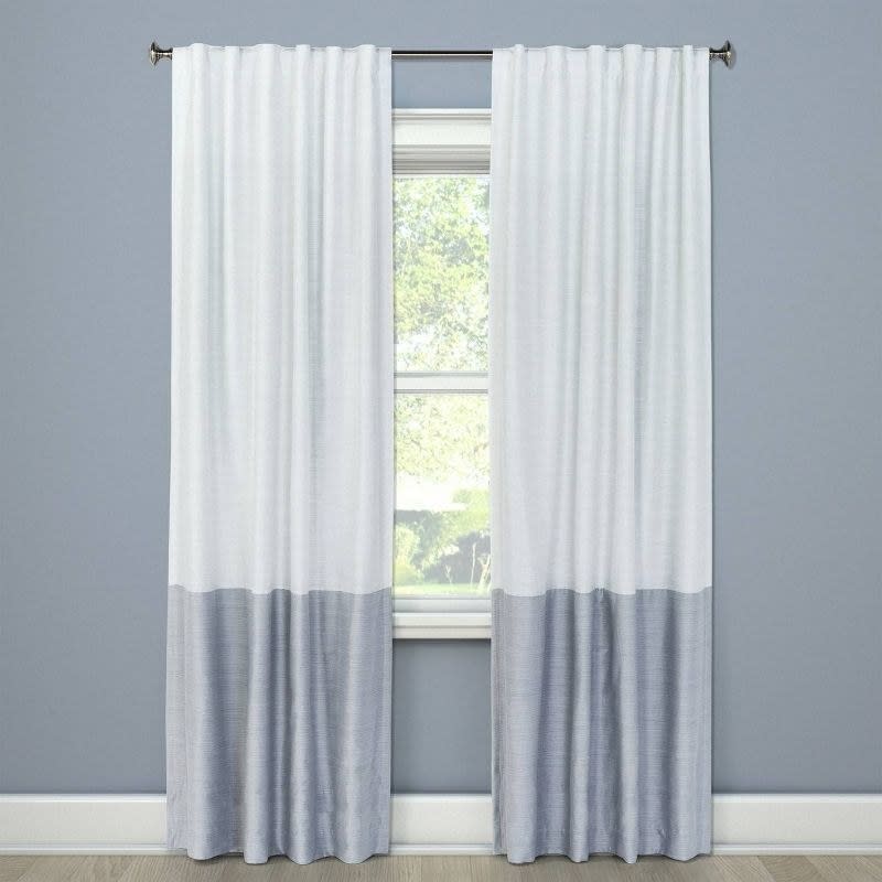 A pair of two-toned curtains, with a lighter shade on top and darker at the bottom, hanging in front of a window