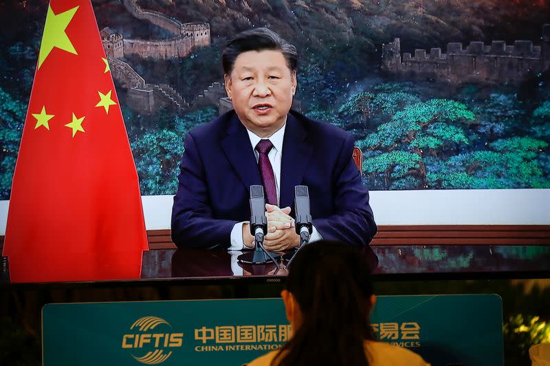 Journalist sits next to a screen showing Chinese President Xi Jinping delivering a speech via video for the opening ceremony of the 2020 China International Fair for Trade in Servic