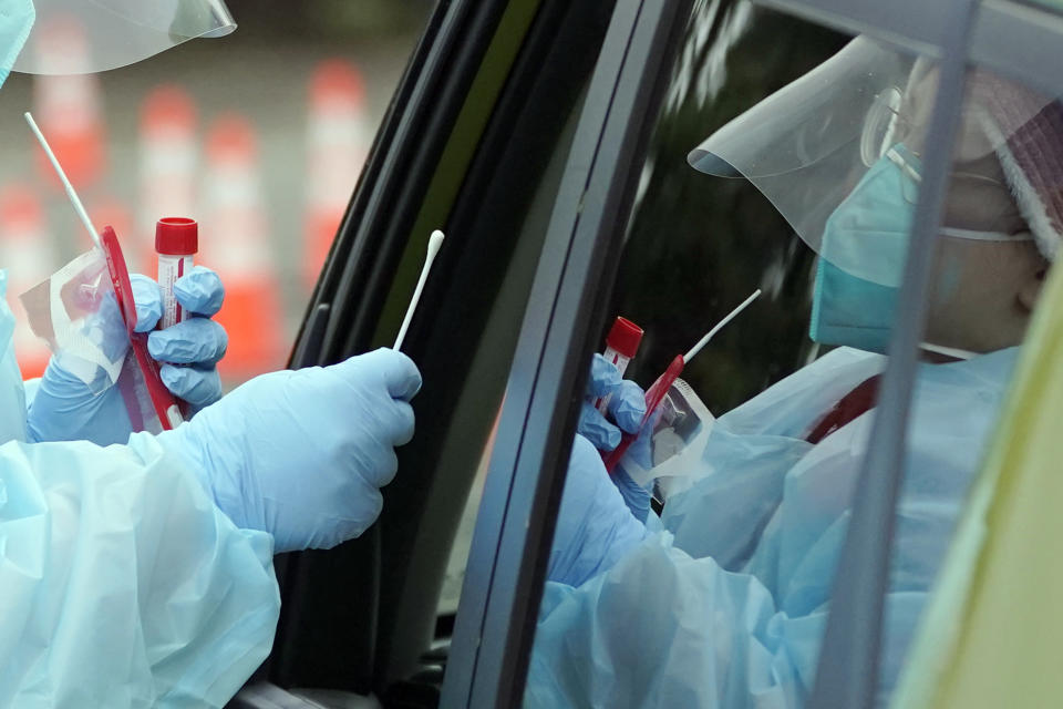 A medical assistant hands a nose swab to a person at a drive-through COVID-19 testing clinic.