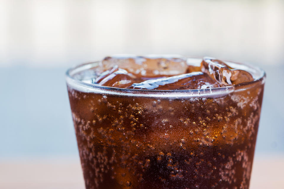 A close-up image of a glass filled with soda and ice cubes. Bubbles can be seen rising to the surface of the drink