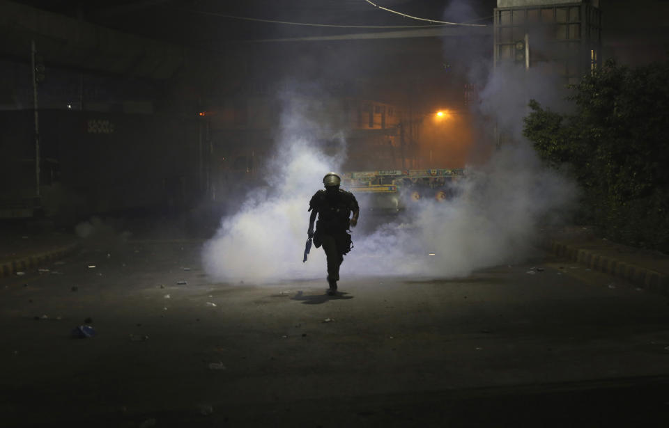 A police officer runs back after fire tear gas shell to disperse the supporters of Tehreek-e-Labiak Pakistan, a radical Islamist political party, marching toward Islamabad, in Lahore, Pakistan, Friday, Oct. 22, 2021. Thousands of Islamists launched their "long march" from the eastern city of Lahore toward Pakistan's capital, demanding that the government release the leader of their Saad Rizvi, who was arrested last year amid demonstrations against France over publishing caricatures of Islam's Prophet Muhammad. (AP Photo/K.M. Chaudary)