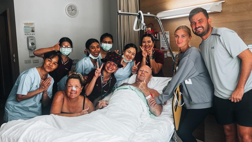 Lee in hospital bed, surrounded by family and nurses. 