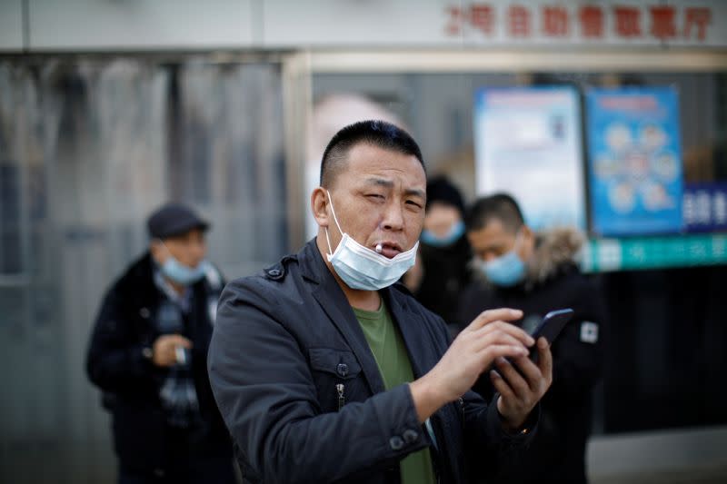 A man wearing a face mask uses his cellphone while smoking outside Beijing Railway Station as the country is hit by an outbreak of the new coronavirus, in Beijing