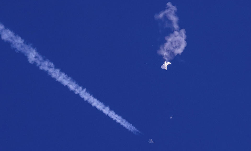 The remnants of a large balloon drift above the Atlantic Ocean, just off the coast of South Carolina, with a fighter jet and its contrail seen below it (Chad Fish via AP)