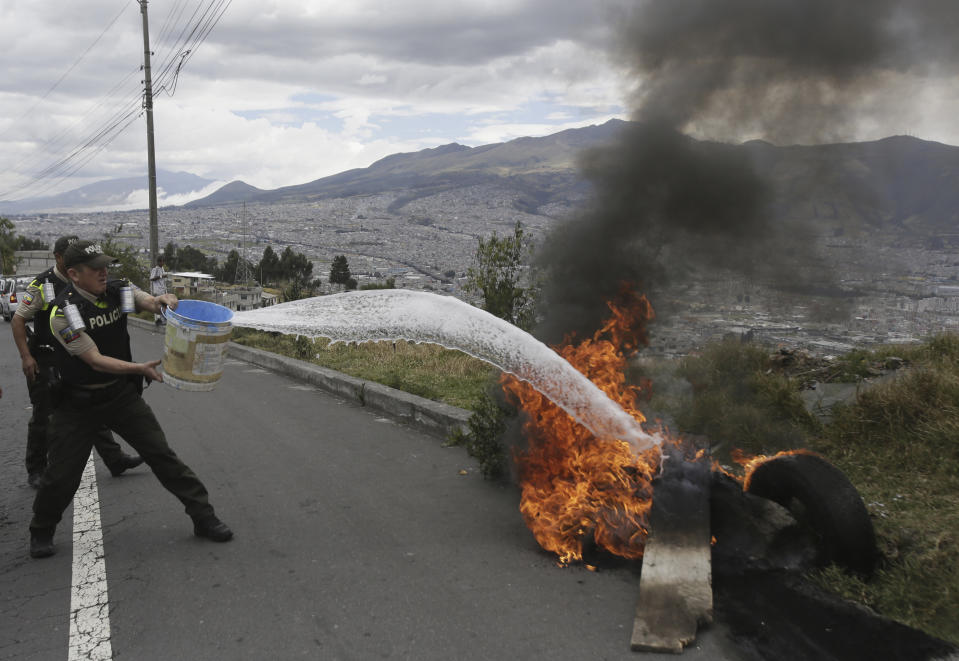Police throws a bucket of water on a burning barricade in Quito, Ecuador, Friday, Oct. 4, 2019, during a nationwide transport strike that shut down taxi, bus and other services in response to a sudden rise in fuel prices. Ecuador's President Lenín Moreno, who earlier declared a state of emergency over the strike, vowed Friday that he wouldn't back down on the decision to end costly fuel subsidies, which doubled the price of diesel overnight and sharply raised gasoline prices. (AP Photo/Dolores Ochoa)