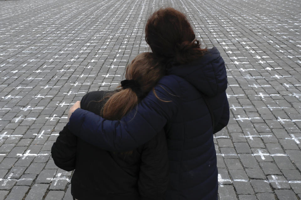 People observe a minute of silence as thousands of crosses are painted at the Old Town Square, to commemorate the 1-year anniversary of the death of first Czech COVID-19 patient, in Prague, Czech Republic, Monday, March 22, 2021. Bells were tolling all across the Czech Republic at Monday noon to honor those who have died of COVID-19 in one of the hardest-hit European Union countries. A 95-year-old man was the first to pass away on March 22, 2020 at Prague's Bulovka hospital. (AP Photo/Petr David Josek)