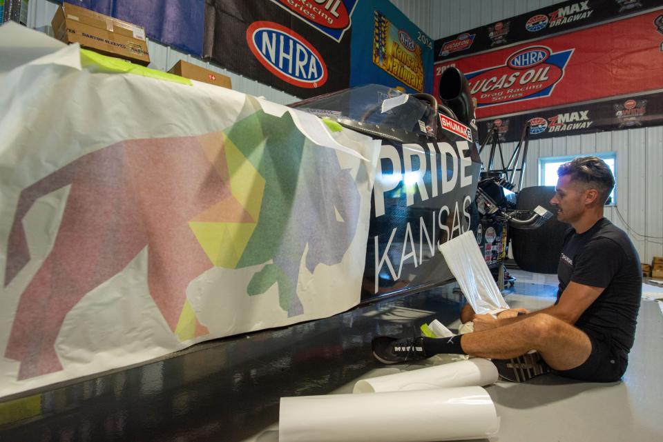 Travis Shumake pulls the vinyl decal to reveal the lettering for the organization Pride Kansas as he works to complete the full rainbow decals on his drag race car Tuesday evening in Spring Hill.