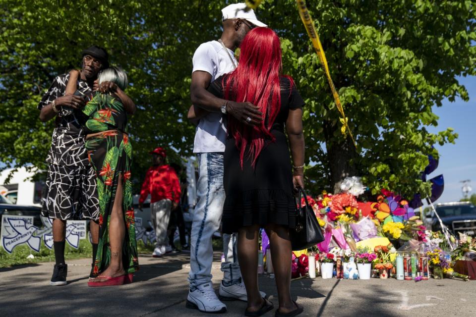 People embrace in front of a sidewalk memorial