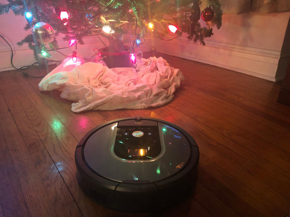 A Roomba on a wood floor below a lit Christmas tree